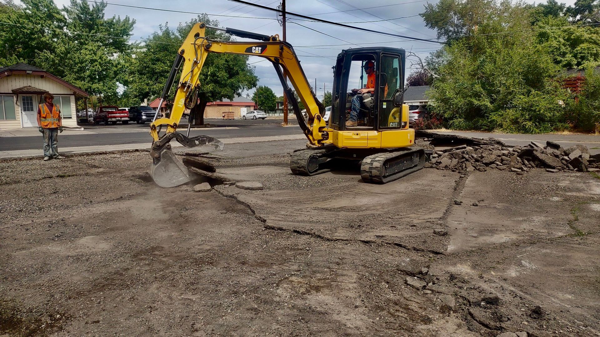 Yellow excavator clearing muddy debris in a flooded area near houses and trees