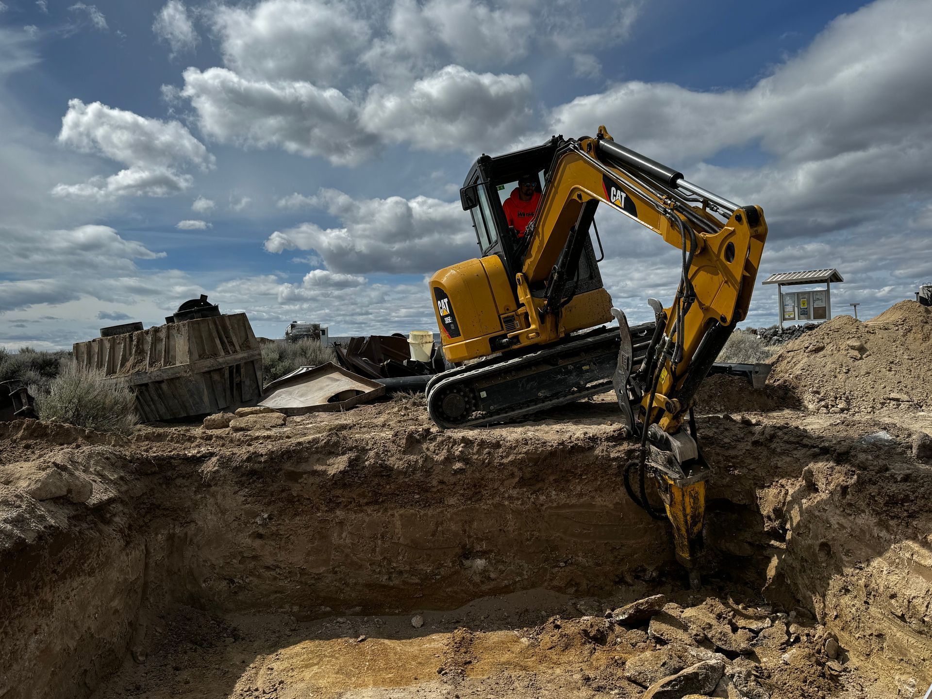 Yellow excavator digging a trench at a construction site under a cloudy sky