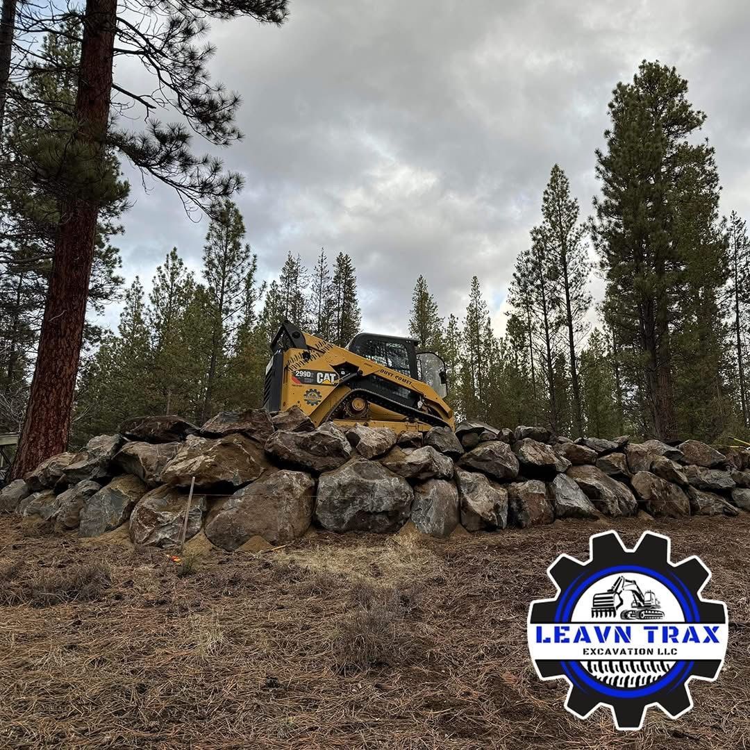 Yellow excavator atop rock pile in a pine forest, with a “Leave No Trace” logo in the corner