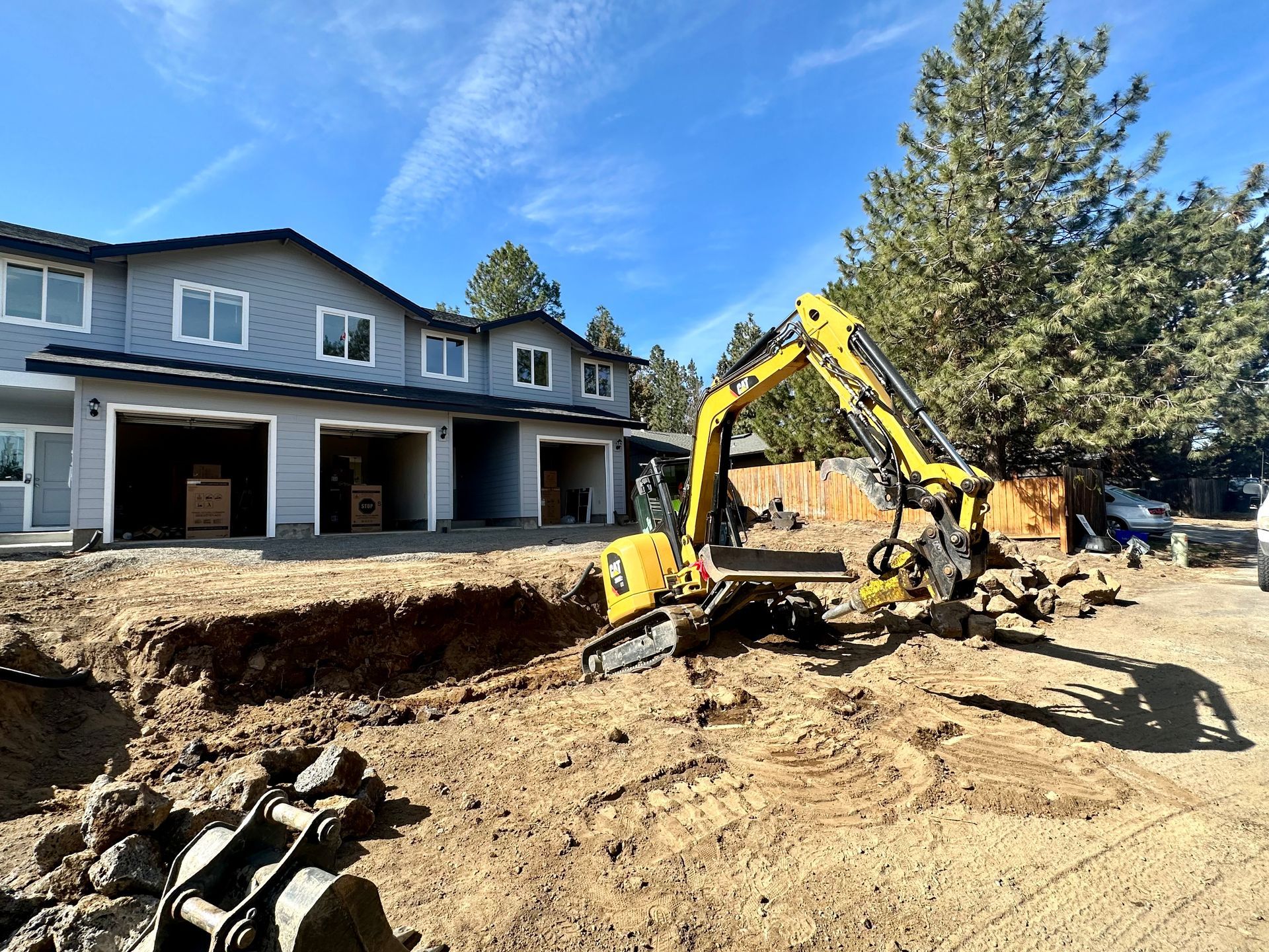 A yellow excavator is digging a hole in the dirt in front of a building.