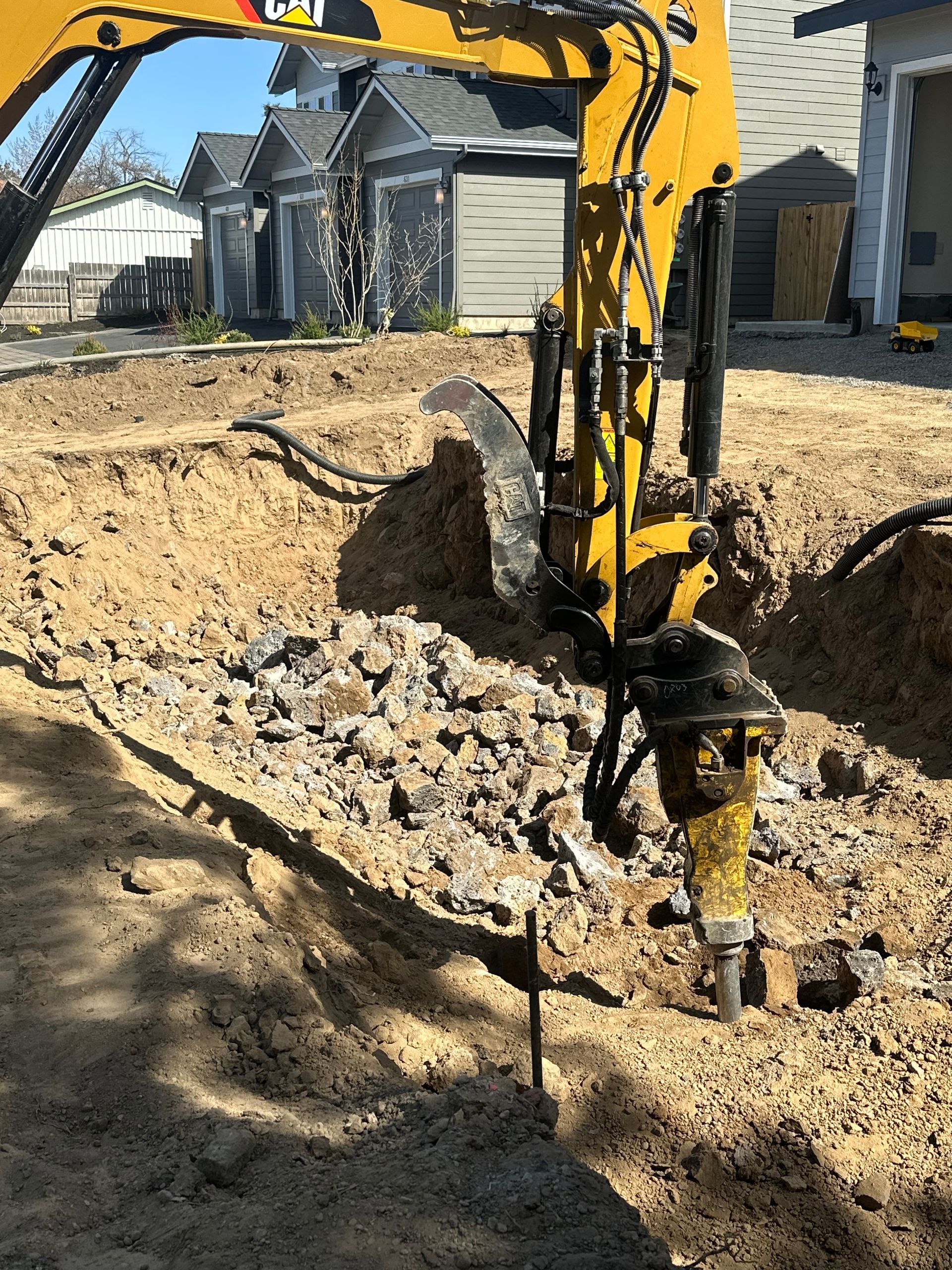 A yellow excavator is digging a hole in the ground in front of a house.