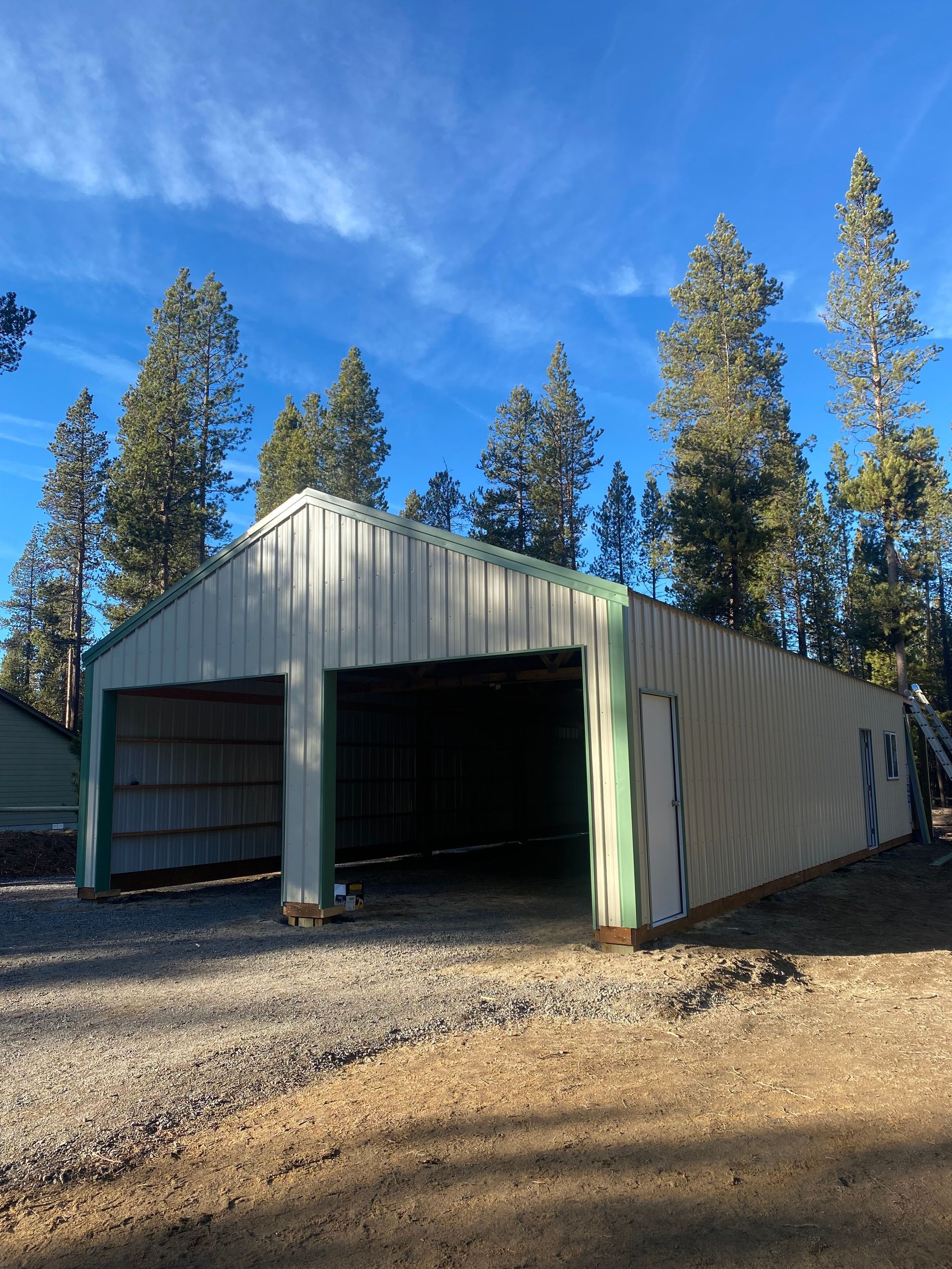 A large metal building with a green trim is surrounded by trees.