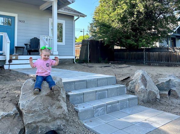 A little girl is sitting on a rock in front of a house.