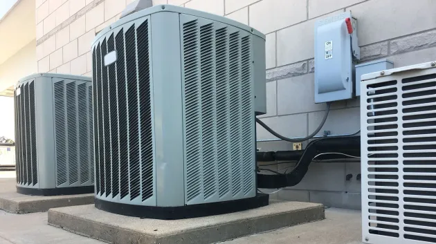 Three outdoor HVAC condenser units beside a building wall, with electrical equipment mounted above.