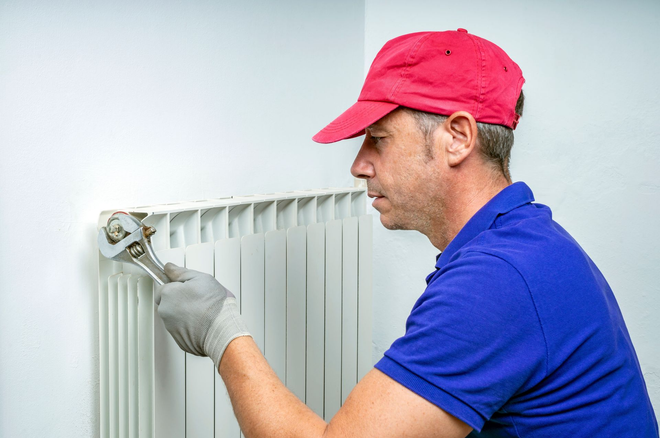 Worker painting a white radiator with a brush, wearing a red cap and blue shirt