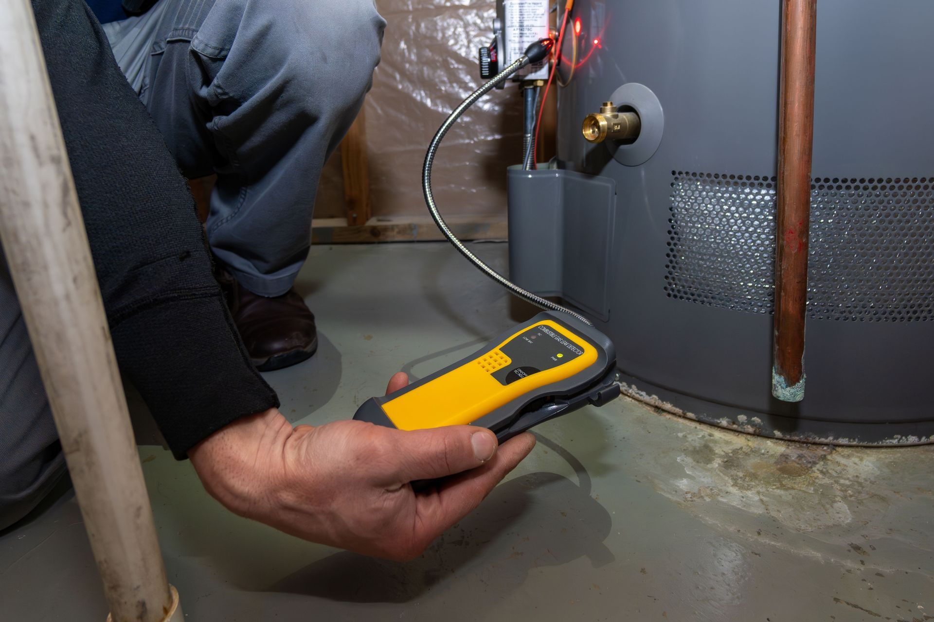 Person uses a handheld leak detector near a water heater base.