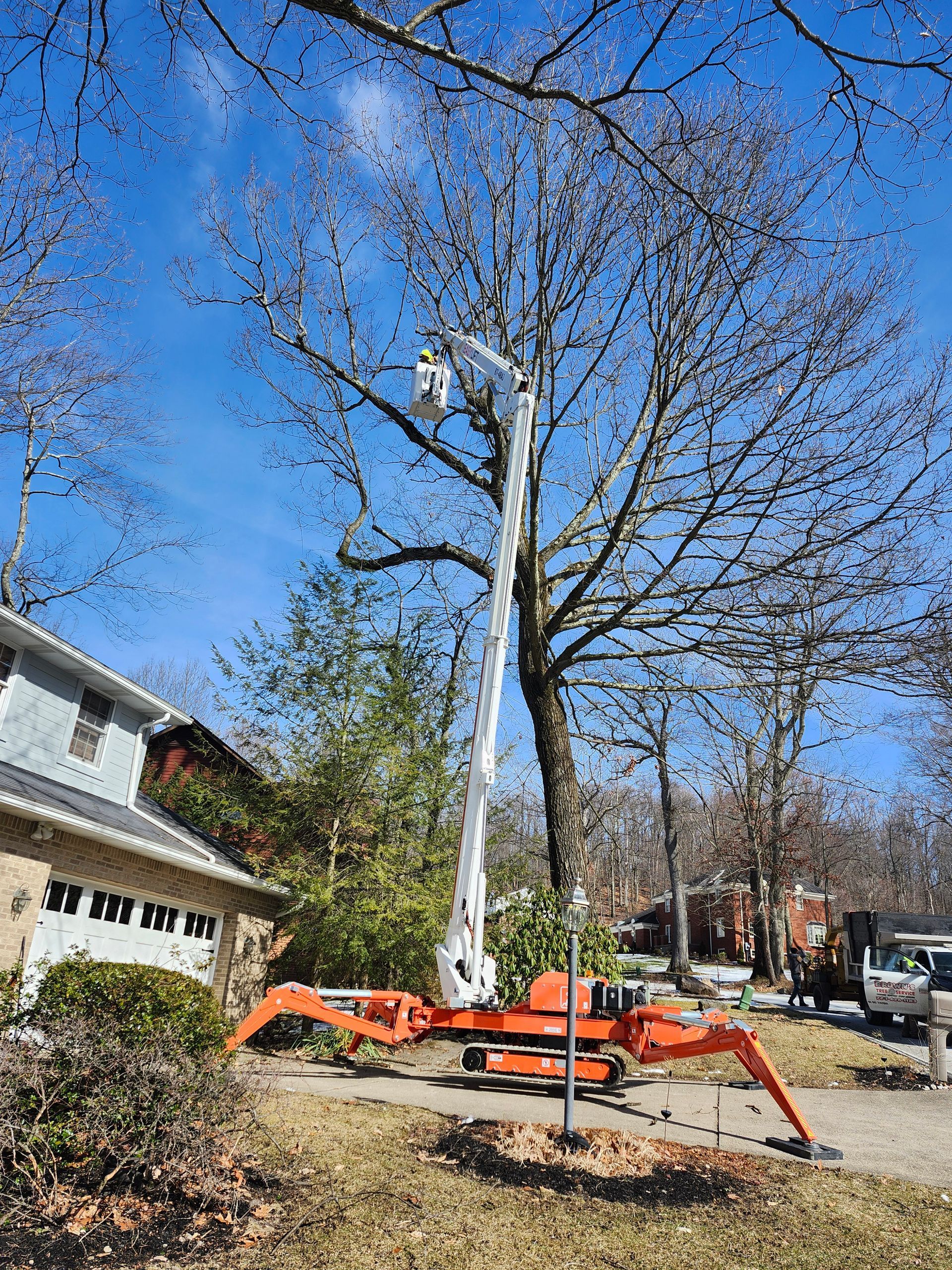 A crane is cutting a tree in front of a house.