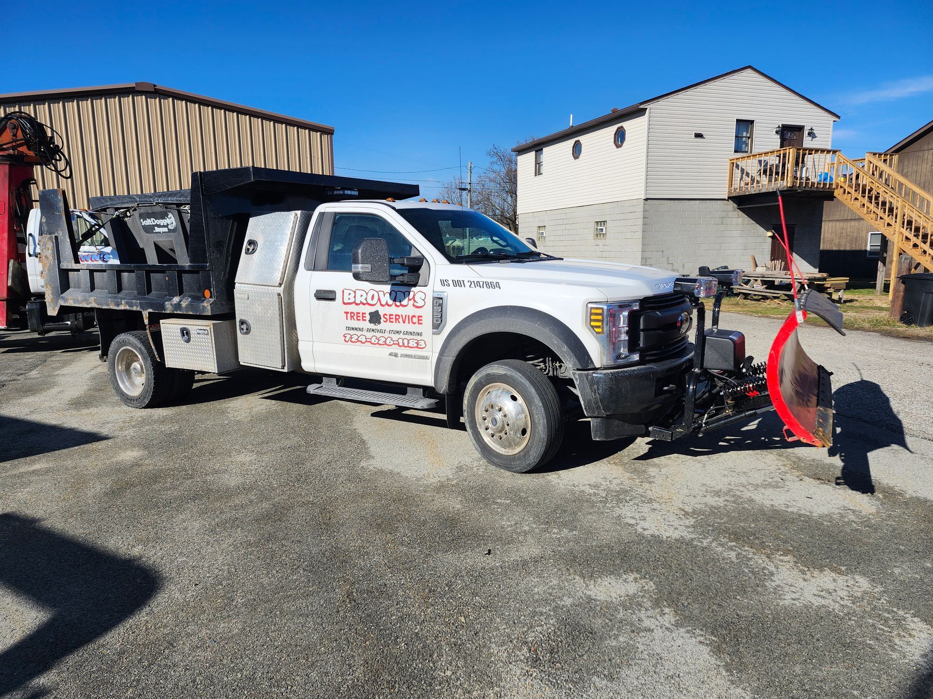 A white truck with a snow plow attached to it is parked in a parking lot.