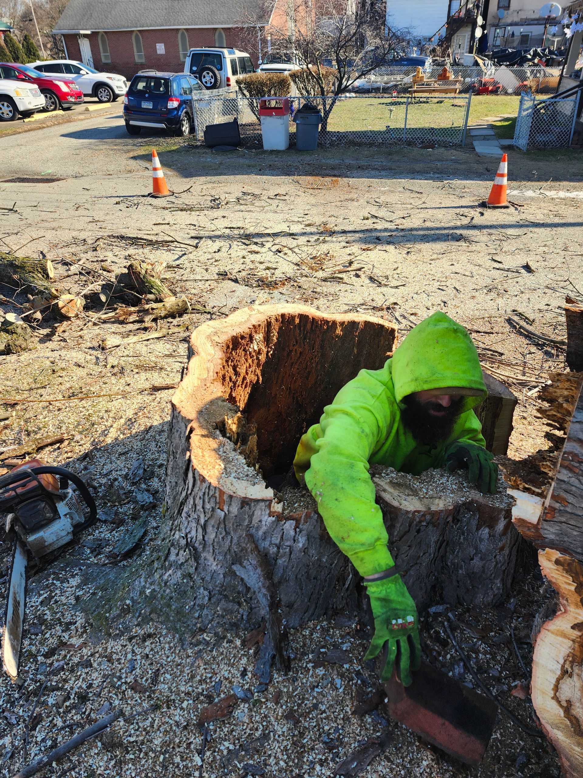 A man in a green jacket is working on a tree stump.