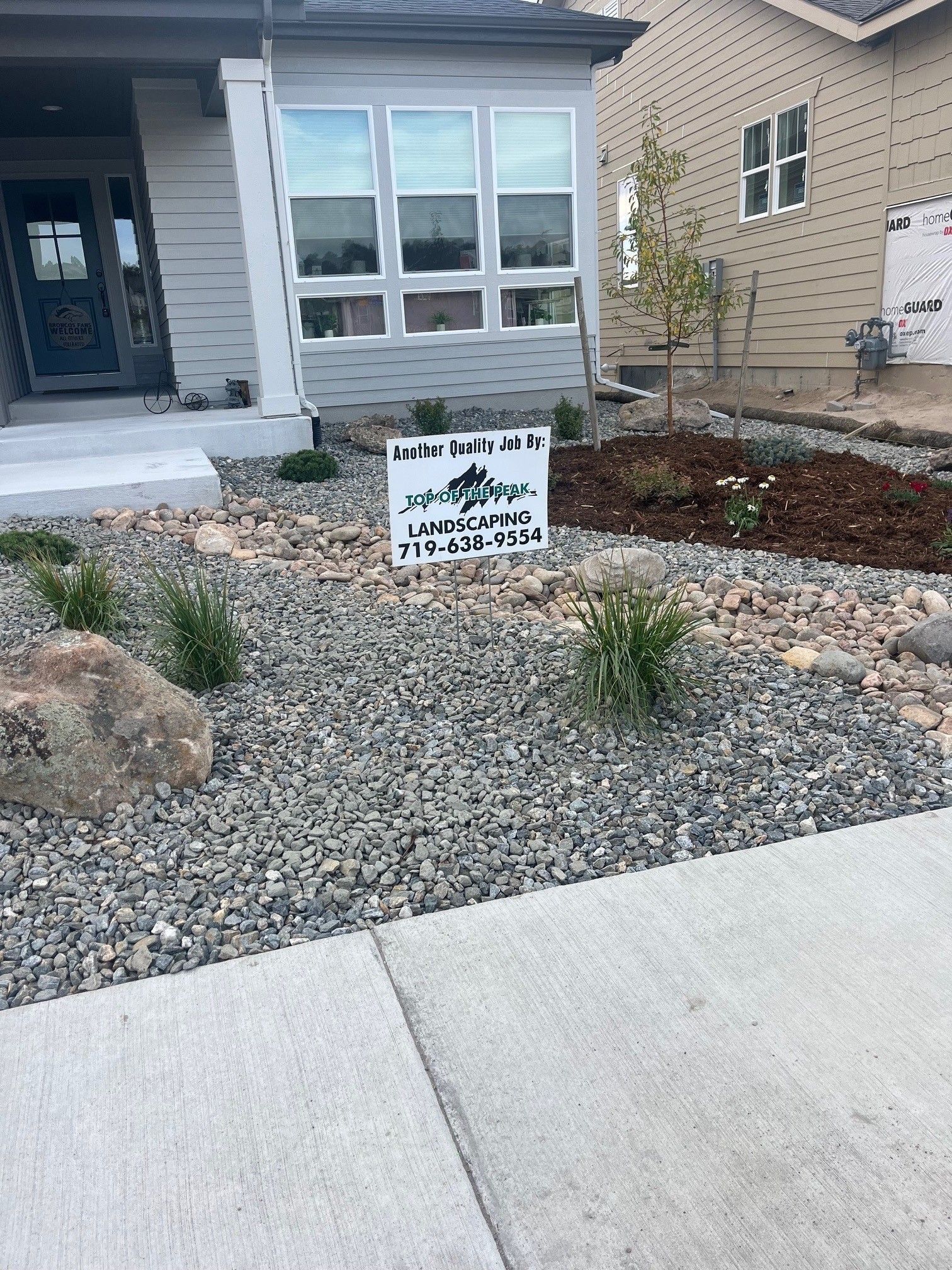 Front yard landscaping with gray gravel, plants, and a sign. A house is in the background.