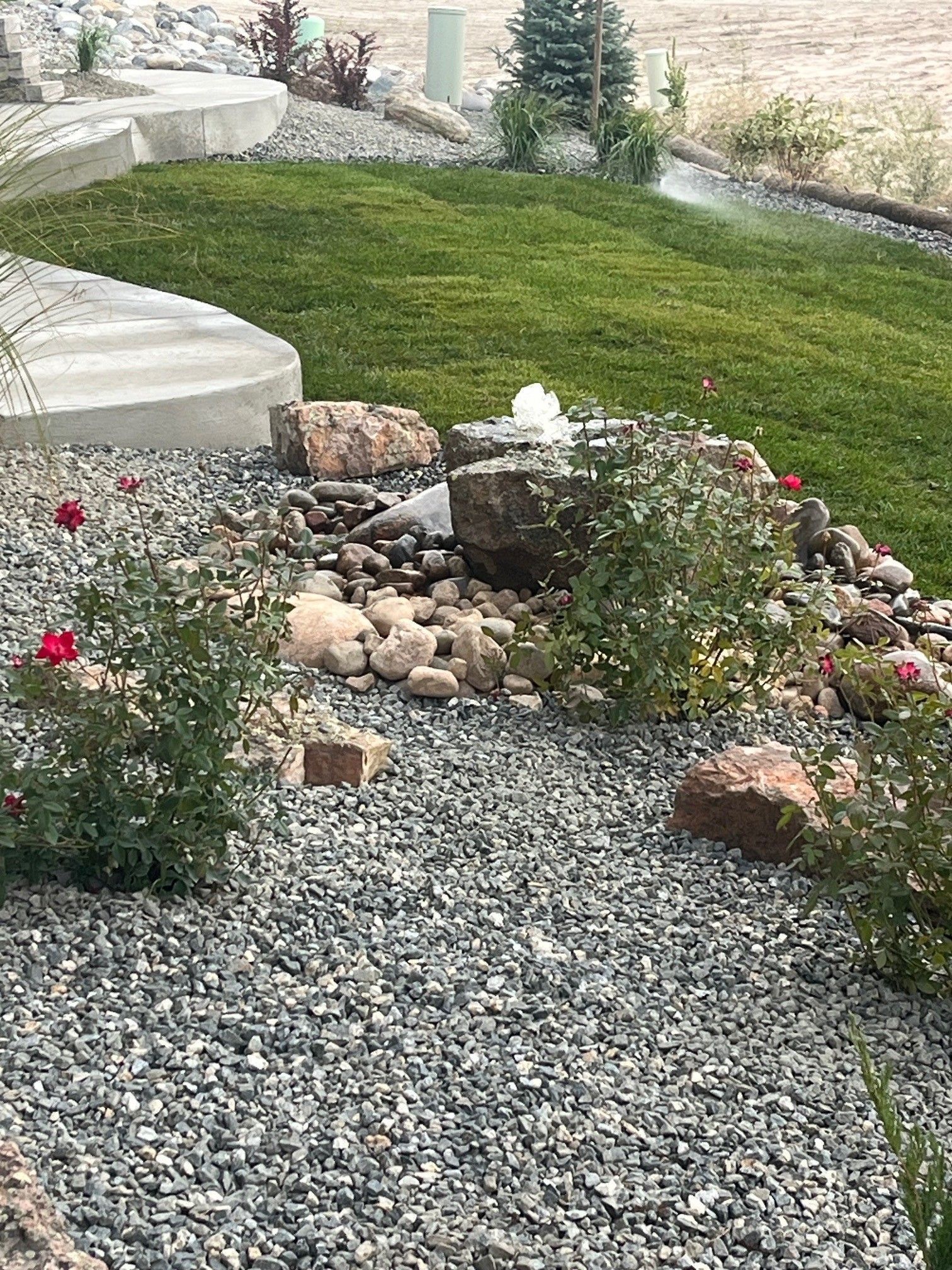 Landscaped yard with a rock fountain, green grass, and gravel.