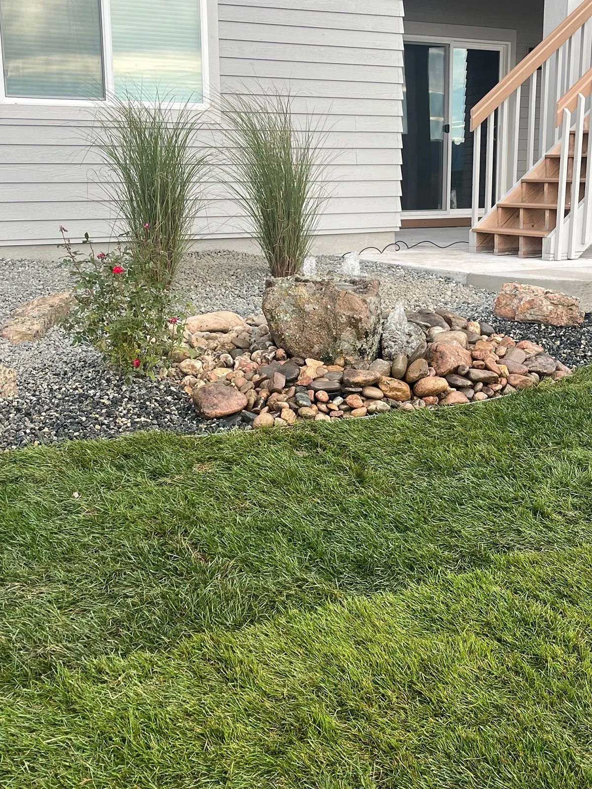 Small water fountain with plants and grass in front of a house.