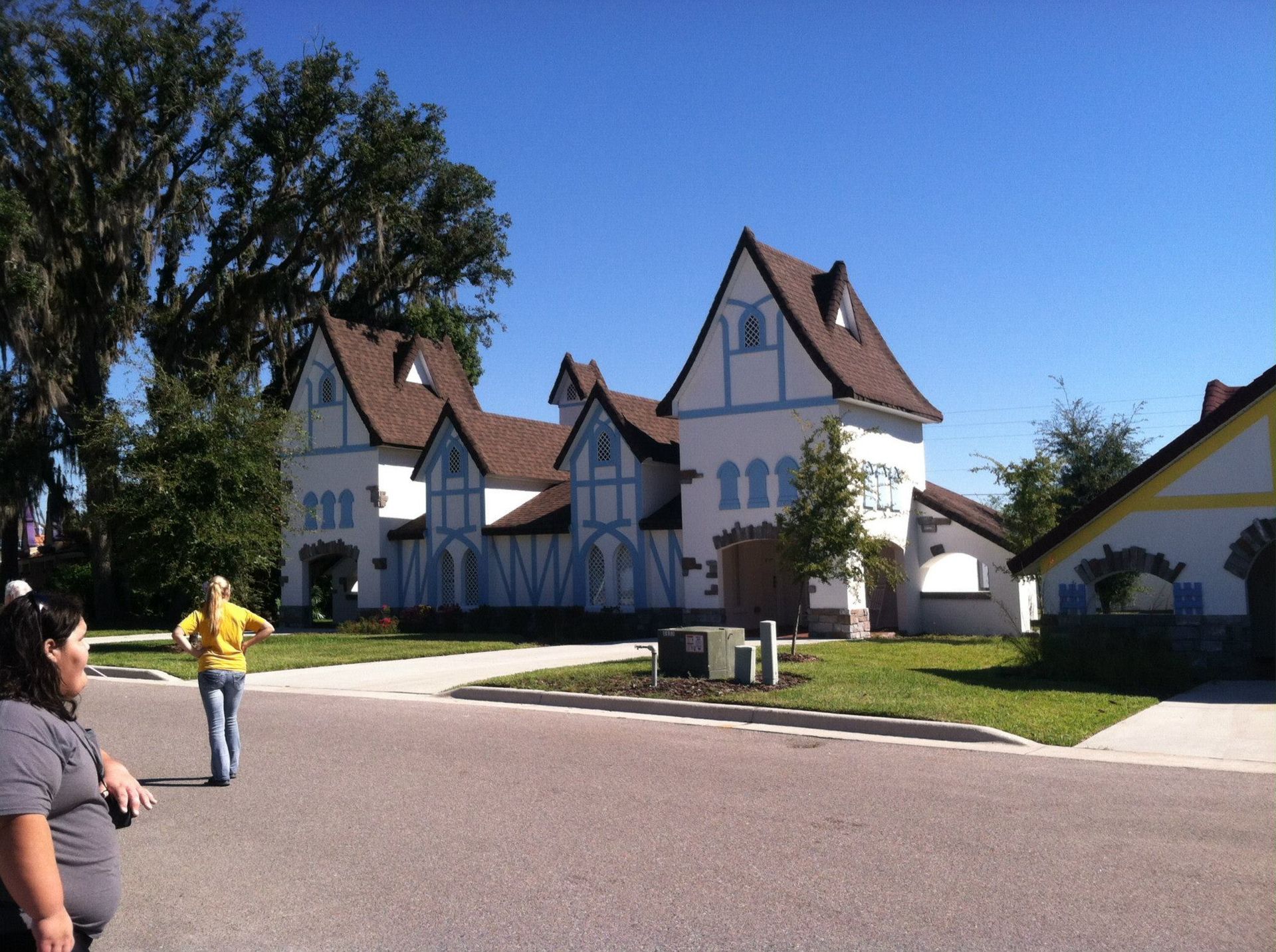 Street view of a whimsical two-story house with blue trim, a person in a yellow shirt walking away.