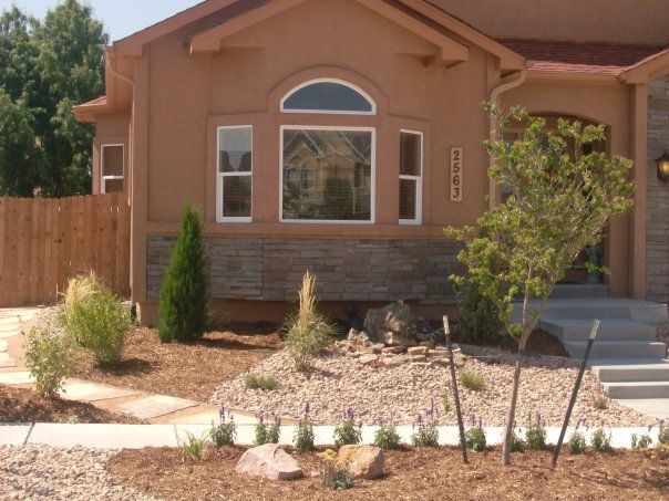 Tan house with stone accents, landscaping, and a walkway.