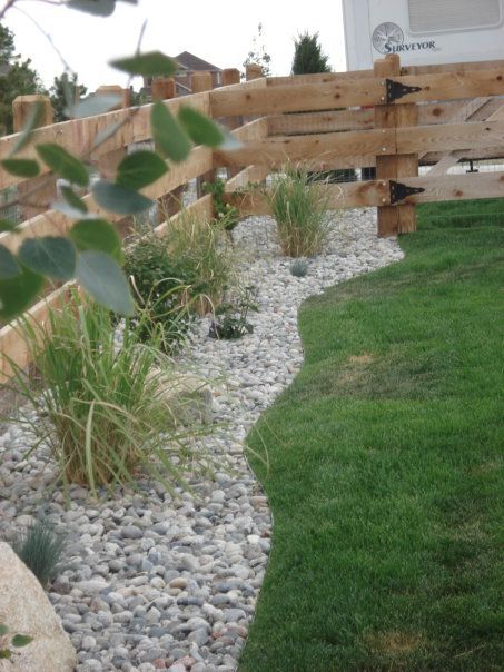 Wooden fence borders a rock garden and green grass.