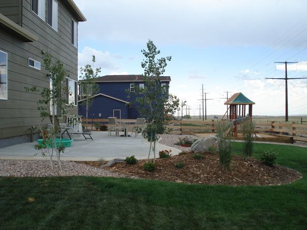 Backyard with a house, patio, playground, and power lines under a cloudy sky.