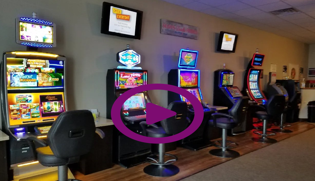Slot machines in a room, with TVs on the wall. The chairs are black and the environment is dim.