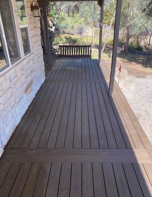 A wooden porch with a bench and a brick building in the background.