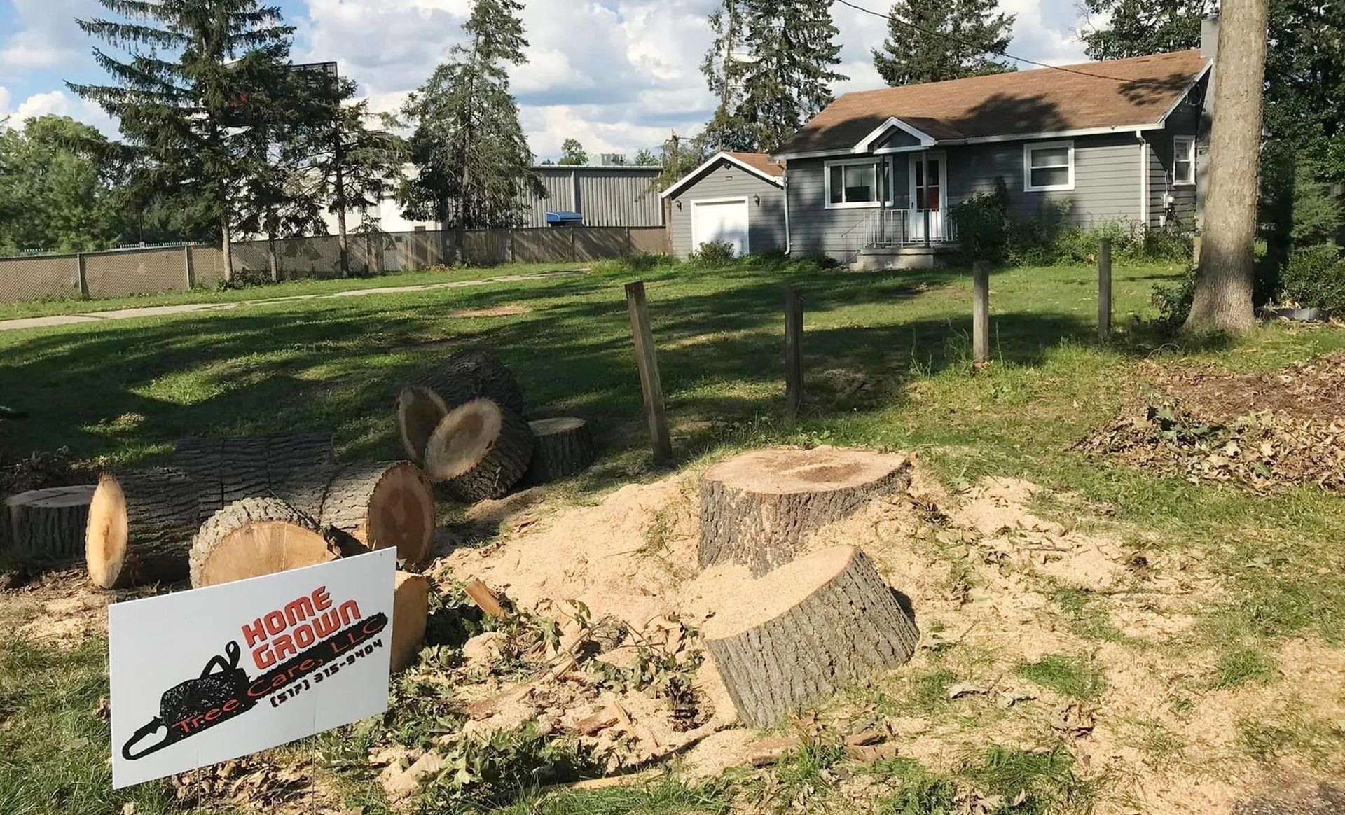 A tree stump in front of a house with a sign that says ' stump grinder ' on it