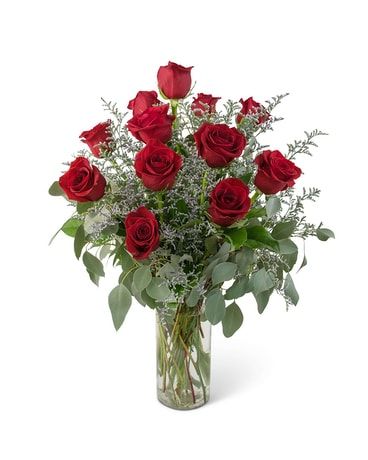 Bouquet of red roses in a clear glass vase, with green and silvery foliage.