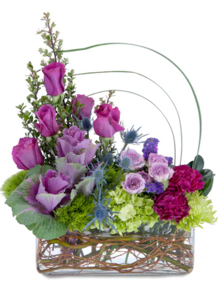 Floral arrangement with purple roses, cabbage, and other blooms in a clear rectangular vase.