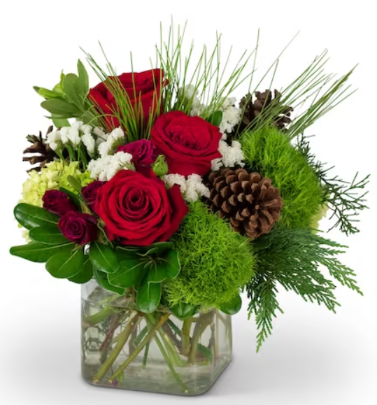 Red roses and greenery arrangement in a square glass vase with pinecones, evoking a festive holiday feel.