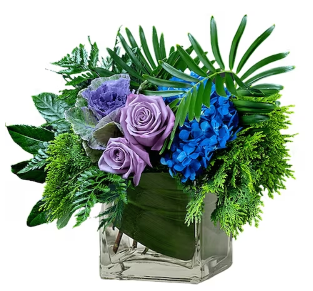 Floral arrangement: Purple roses and blue hydrangea in a clear glass square vase with greenery.
