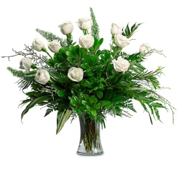 White roses in a glass vase, surrounded by green foliage.
