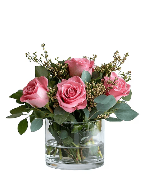 A vase filled with pink roses and greenery on a white background.