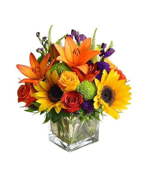 Colorful fall flower arrangement in a square glass vase. Includes lilies, sunflowers, roses, and greenery.