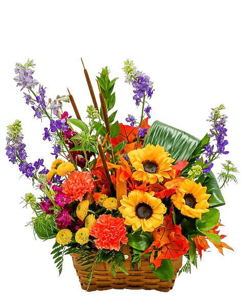 A basket overflowing with colorful flowers, including sunflowers and purple delphiniums, against a white backdrop.