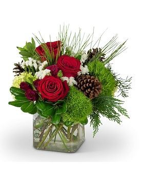 Floral arrangement in a square glass vase with red roses, greenery, and pinecones.