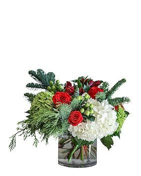 Floral arrangement in a glass vase: red roses, white hydrangeas, evergreen branches.