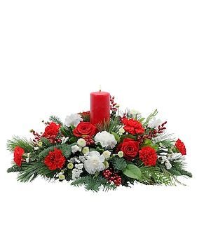 Christmas centerpiece: Red candle surrounded by red and white flowers, evergreen, and berries.