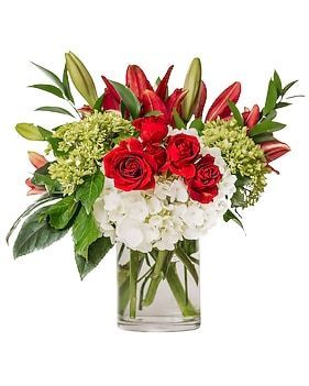 Bouquet of red roses, lilies, and white hydrangeas in a glass vase.