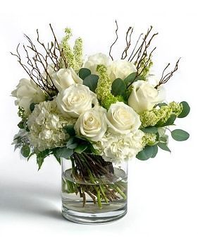 White roses, hydrangea, and branches in a clear glass vase.