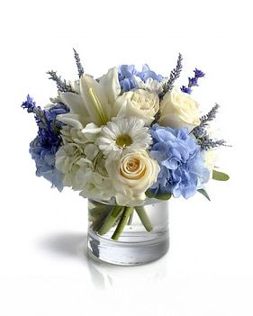 Blue and white floral arrangement in a clear glass vase. Includes roses, hydrangea, and lilies.