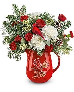 Red pitcher holds a Christmas floral arrangement with carnations, roses, pine, a cardinal ornament, and pinecones.
