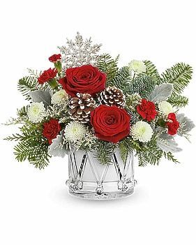 Christmas floral arrangement in a drum-shaped glass vase with red roses, pine cones, and greenery.