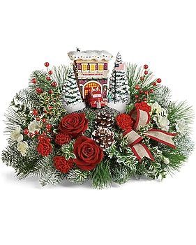 Christmas centerpiece with roses, greenery, miniature building, and ribbon.