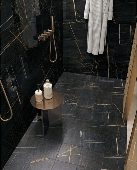A bathroom with black tiles and a white robe hanging on the wall