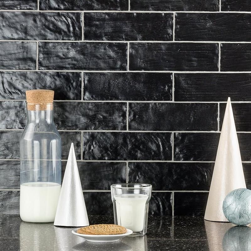 A bottle of milk and a glass of milk are on a counter in front of a black tile wall.
