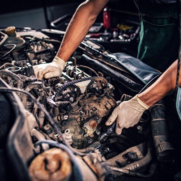 A mechanic wearing gloves works on an open car engine in a repair shop.