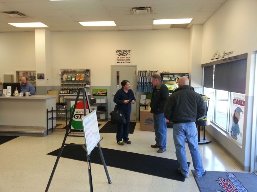Three people talk in a brightly lit automotive service center lobby with shelves of products and service posters.