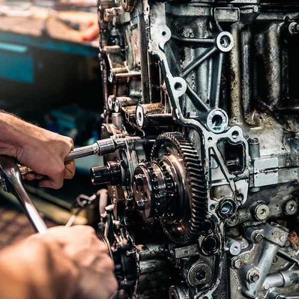 A mechanic uses a ratchet to work on the complex, metallic gears of an exposed car engine in a repair shop.
