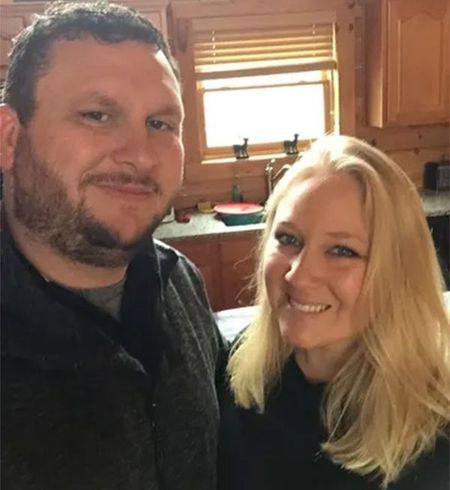 Two smiling people posing together in a sunlit kitchen.