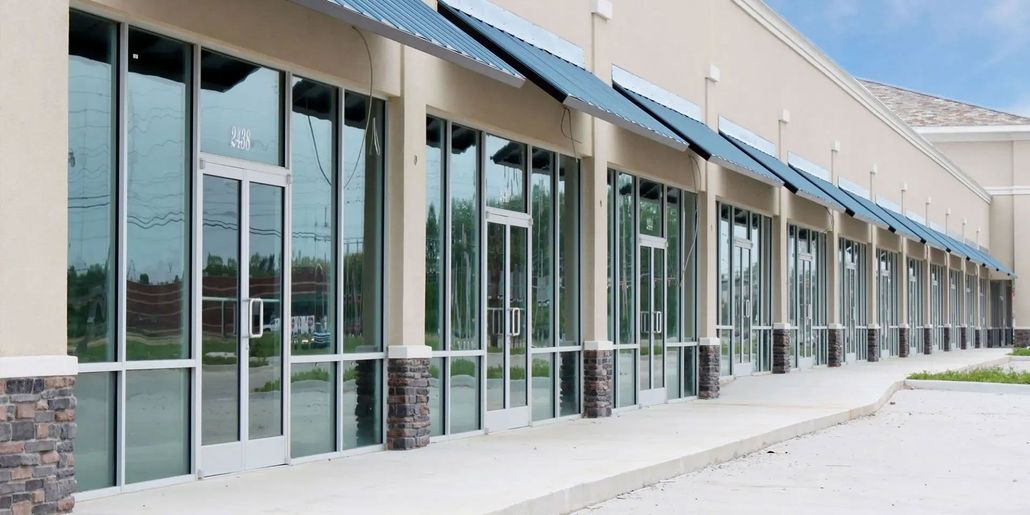 Storefront with large glass windows and blue awnings along a modern strip mall walkway
