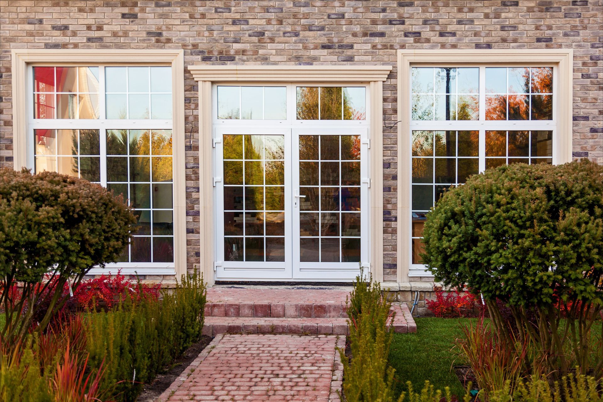 Brick house front entrance with white double doors, large windows, and a landscaped walkway.