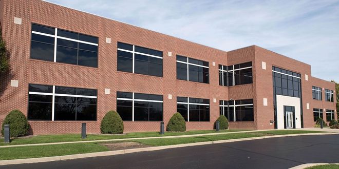 Two-story red-brick office building with large windows and a small landscaped lawn