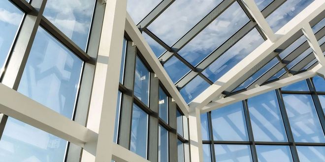 Glass atrium ceiling with steel beams and blue sky visible through large windows